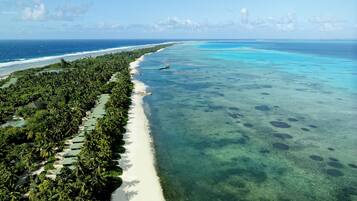 An aerial view of a beach with clear turquoise waters, a sandy shoreline, and dense tropical vegetation.