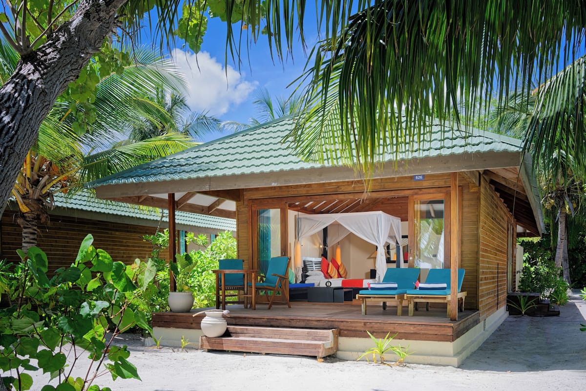 A wooden bungalow with a covered porch, outdoor seating, and lush tropical vegetation.