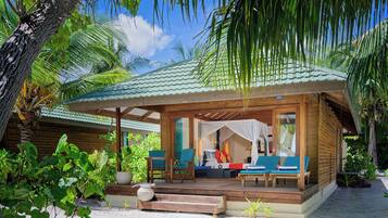Una cabaña de madera con porche cubierto, mobiliario exterior y exuberante vegetación tropical.