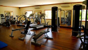 Une salle de sport équipée de divers appareils d’exercice, dotée d’un plancher en bois et de grandes fenêtres.