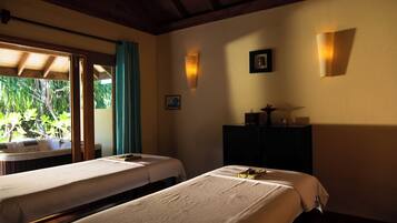 Two single beds with white bedspreads, a dresser, and a table with a lamp.