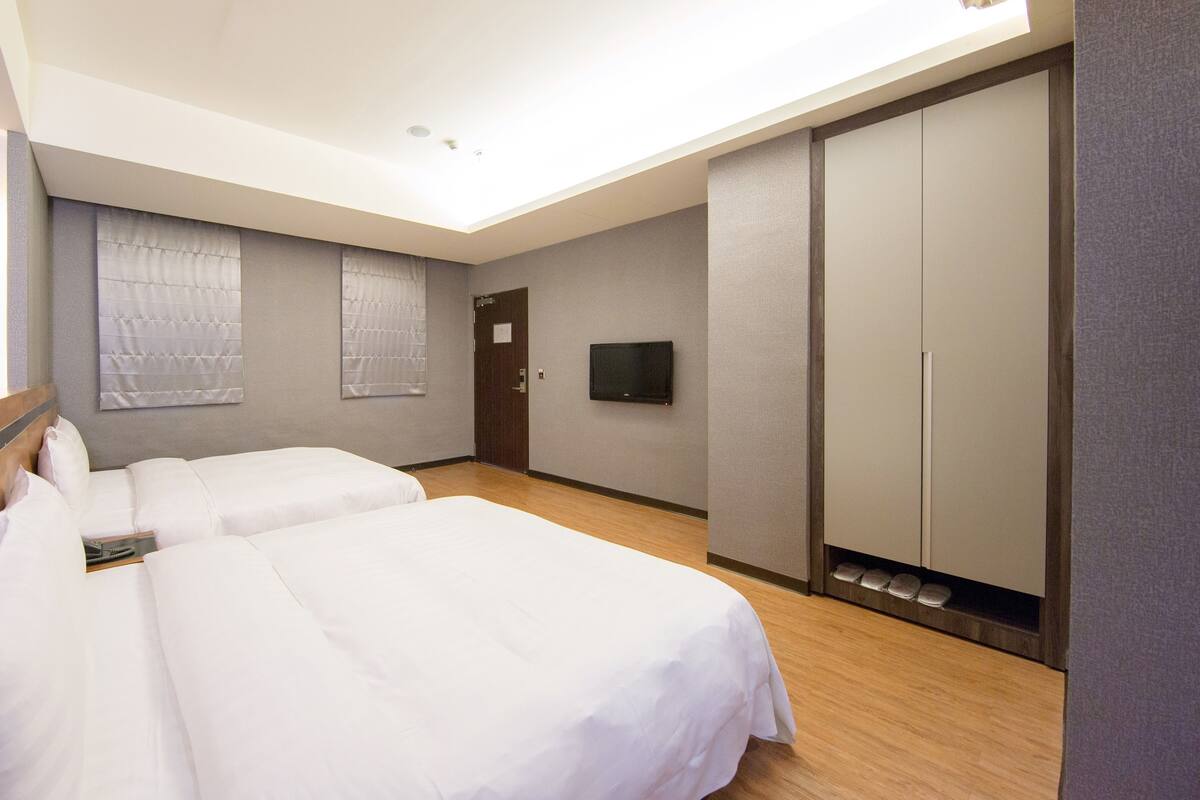 Een hotelkamer met twee bedden, een kledingkast, een televisie en een plafondlamp.