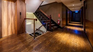 Un interior moderno con una escalera de madera, un extintor y un pasillo que conduce a una puerta.
