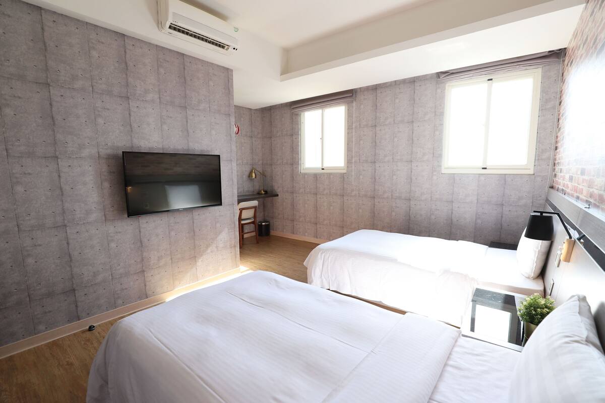 Een moderne hotelkamer met twee bedden, een flatscreen-tv aan de muur en grote ramen die voor natuurlijk licht zorgen.