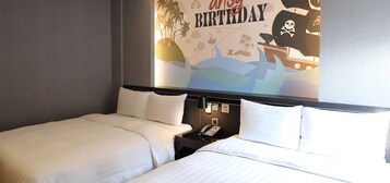A hotel room with two beds, a nightstand with a phone, and a wall mural with a birthday theme.