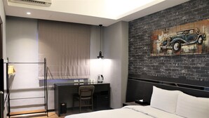 Habitación de hotel con cama, escritorio y silla, lámpara, y pared de ladrillo con un mural de un coche antiguo.