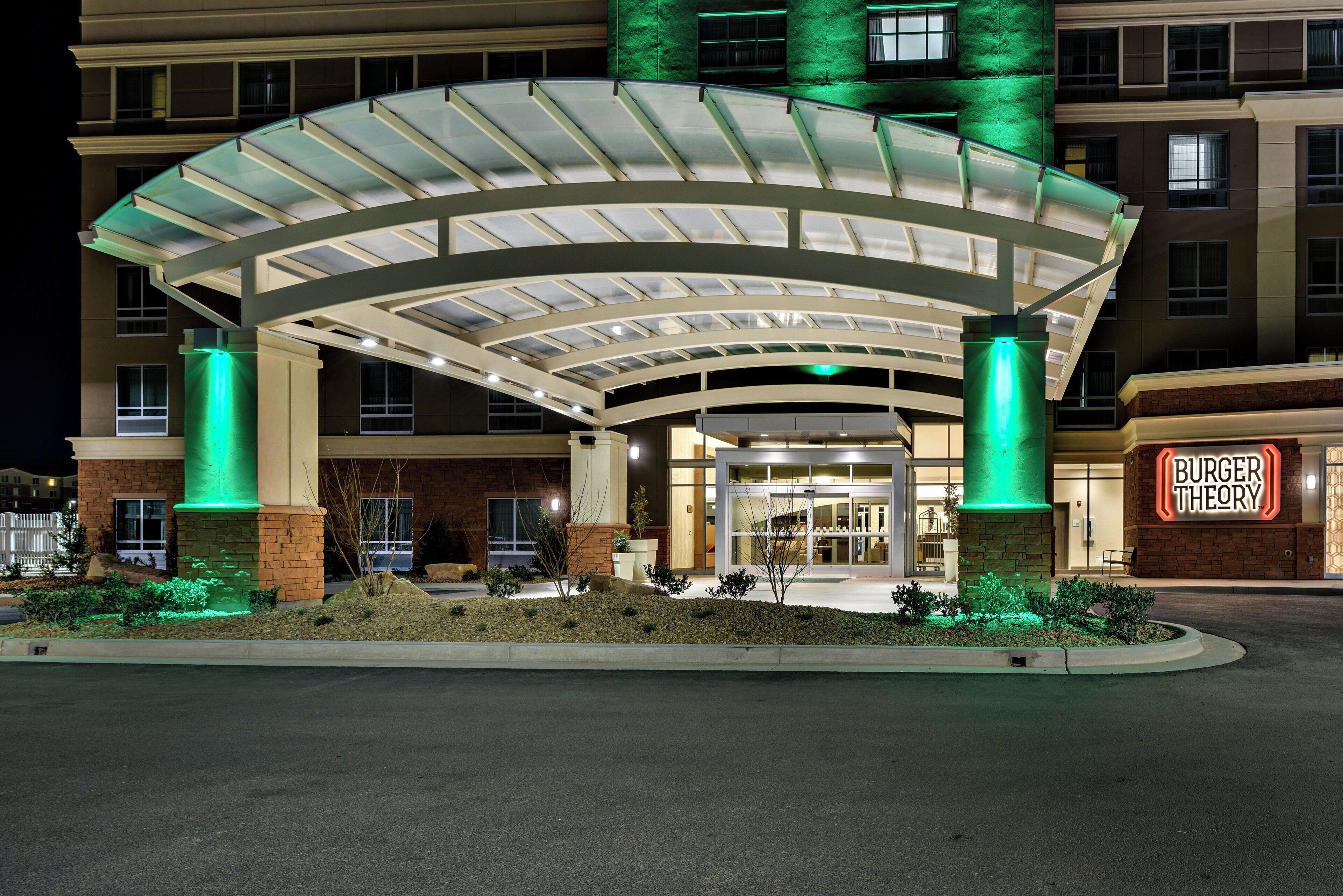 A hotel entrance with a covered walkway, a Burger Theory sign, and a landscaped area with shrubs.