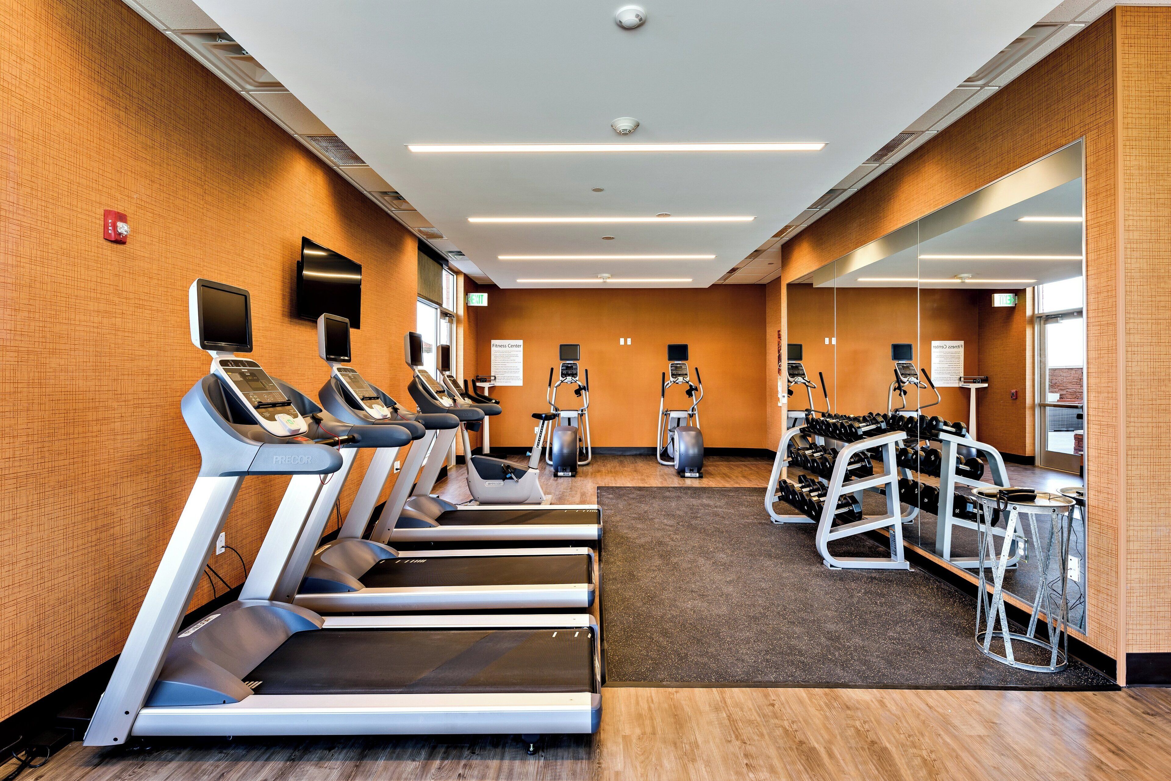 Un gimnasio con cintas de correr, elípticas y un rack de pesas.