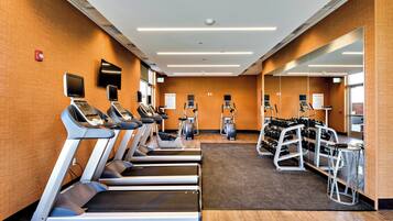 Un gimnasio con cintas de correr, elípticas y un rack de pesas.