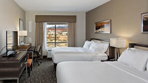 A hotel room with two beds, a desk, a chair, a lamp, and a window with a mountain view. - Holiday Inn St. George Conv Ctr by IHG (St. George)
