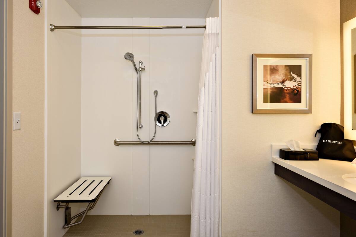 A shower with a grab bar, a bench, and a framed picture on the wall.