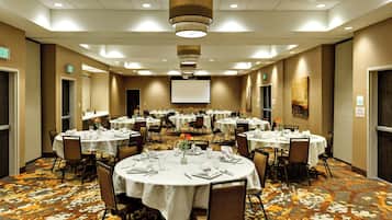 Une salle de conférence équipée de plusieurs tables dressées pour un repas, avec des chaises, des tables et un écran de projection.