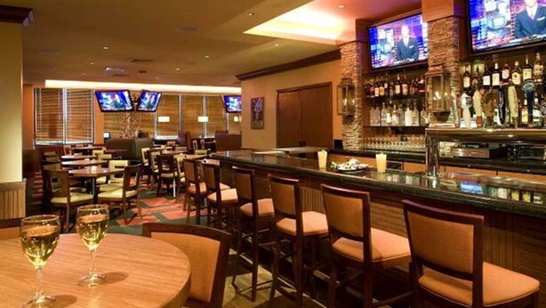 A bar area with multiple seating options, including round tables and bar stools, and a well-stocked bar with various bottles. - Holiday Inn St. George Conv Ctr by IHG (St. George)