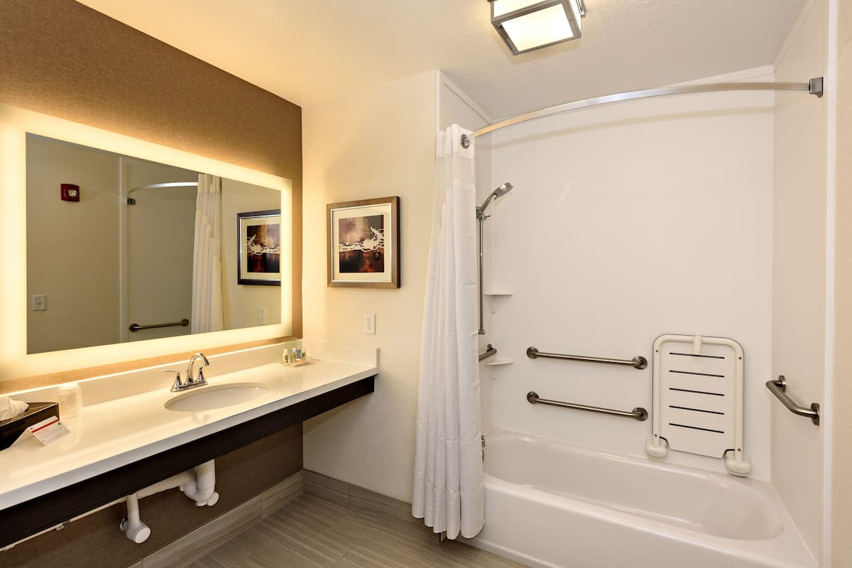 A bathroom with two sinks, a large mirror, a shower with grab bars, and a towel rack.