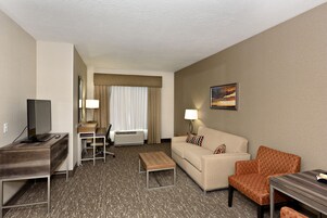 Una habitación de hotel con escritorio, sofá, mesa de centro y televisor.
