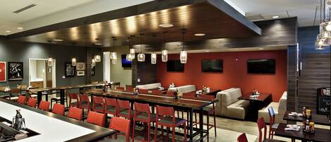 A modern restaurant with a long communal table, individual booths, and red chairs.