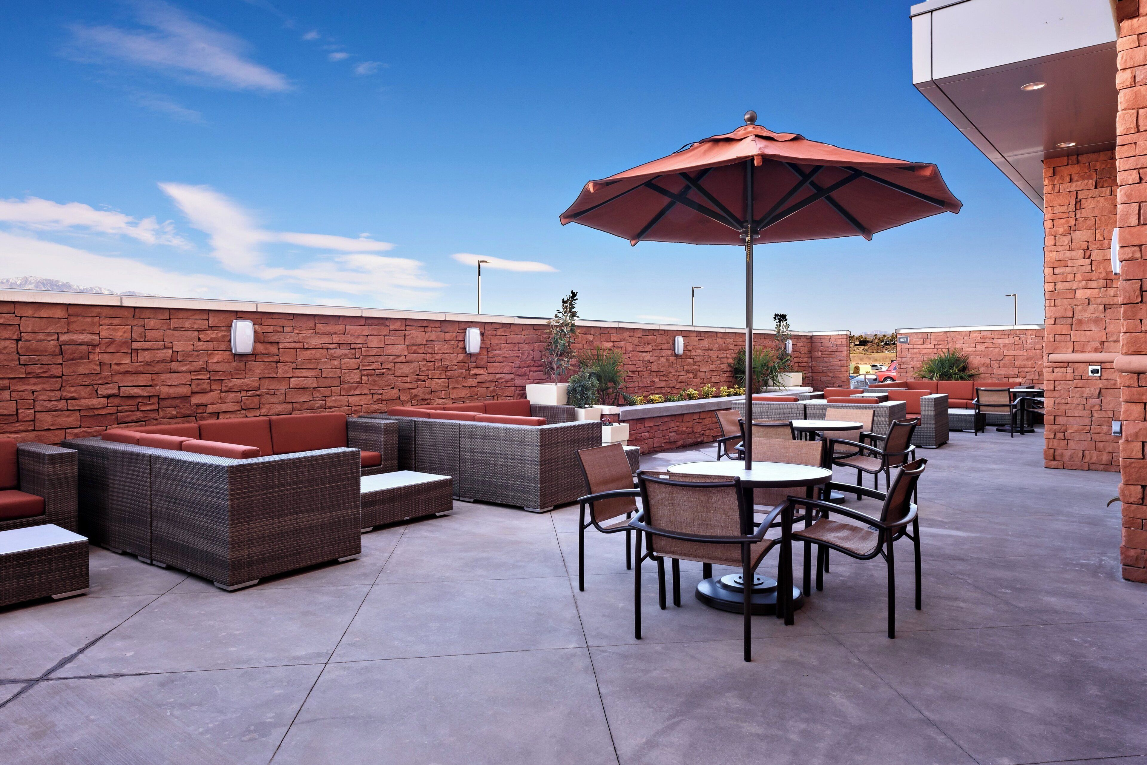 Un patio al aire libre con mobiliario, mesas y una sombrilla.