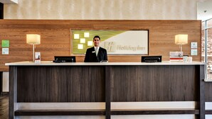 A hotel reception desk with a wooden panel backdrop, a nameplate, and a sign reading "Holiday Inn". - Holiday Inn St. George Conv Ctr by IHG (St. George)