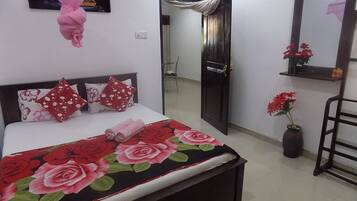 A bedroom with a bed, a door, a mirror, and a vase with flowers.