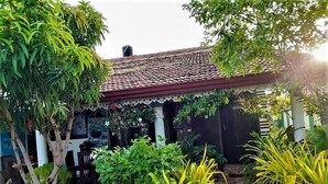 Een traditioneel huis met pannendak, omringd door weelderig groen en plantenpotten.
