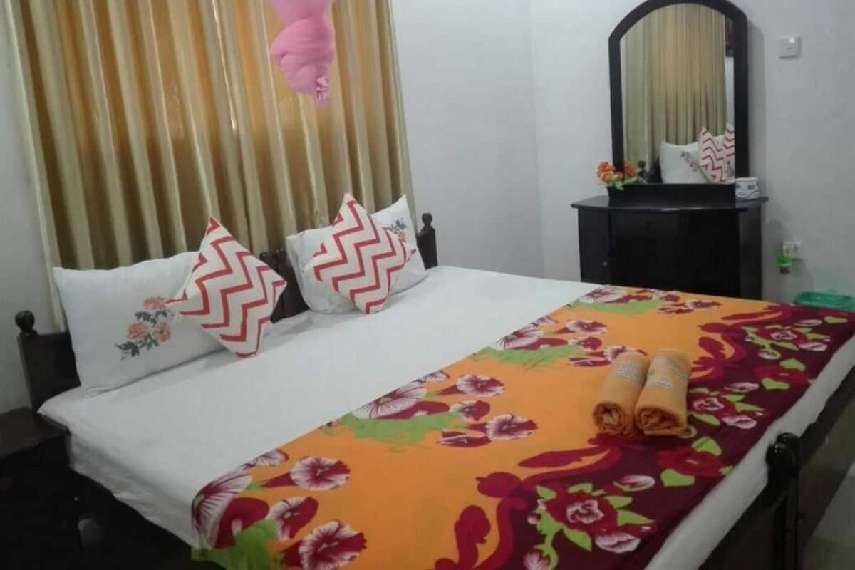 A neatly made bed with floral bedding, a mirror on a dark wooden side table, and a curtain with a pink canopy.