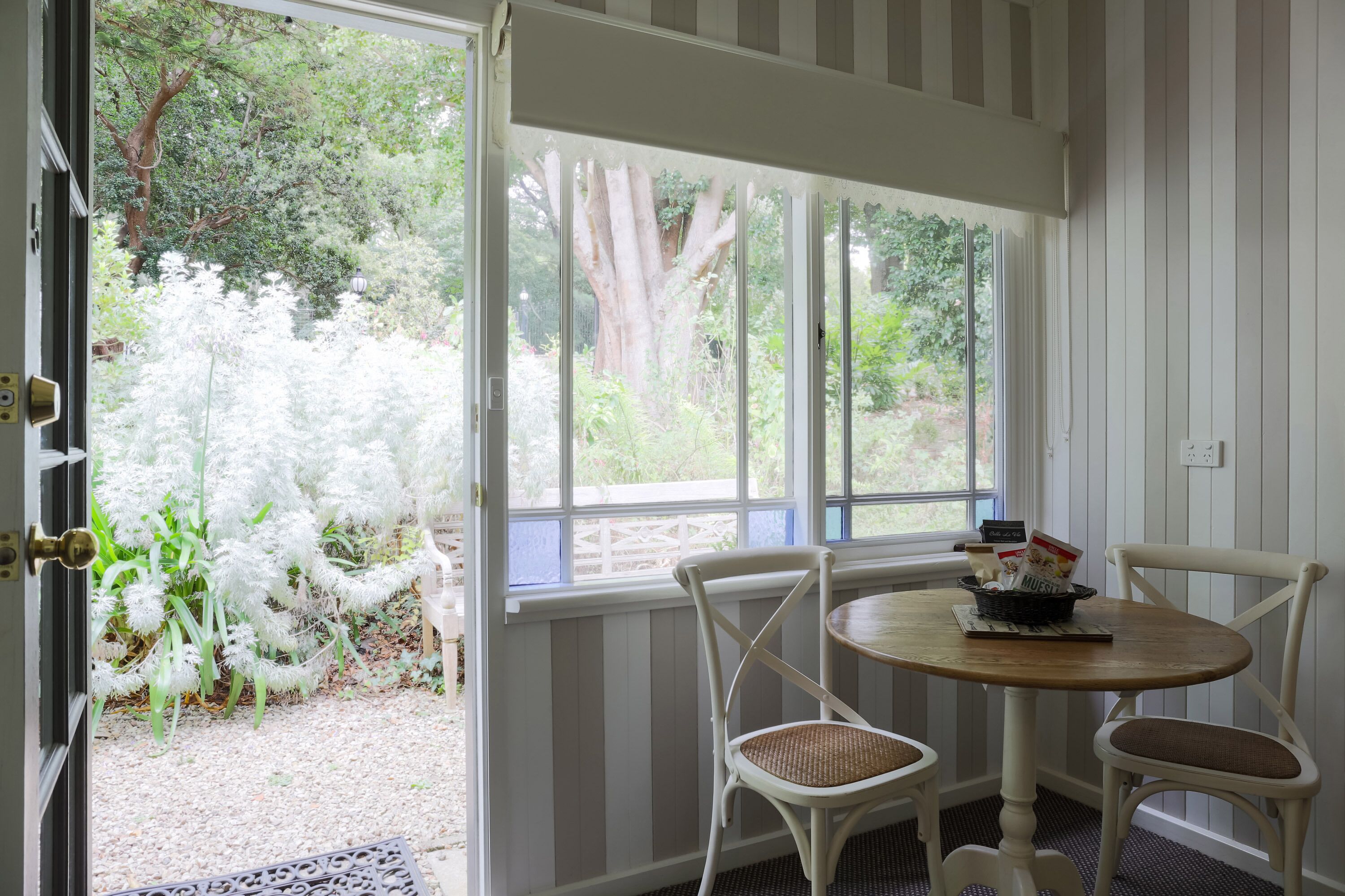 A room with a dining table and chairs, a window with a view of greenery, and a door leading outside.