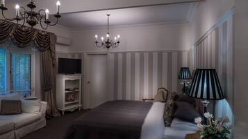 A hotel room with a large bed, a TV, a chandelier, striped wallpaper, and a window with curtains.