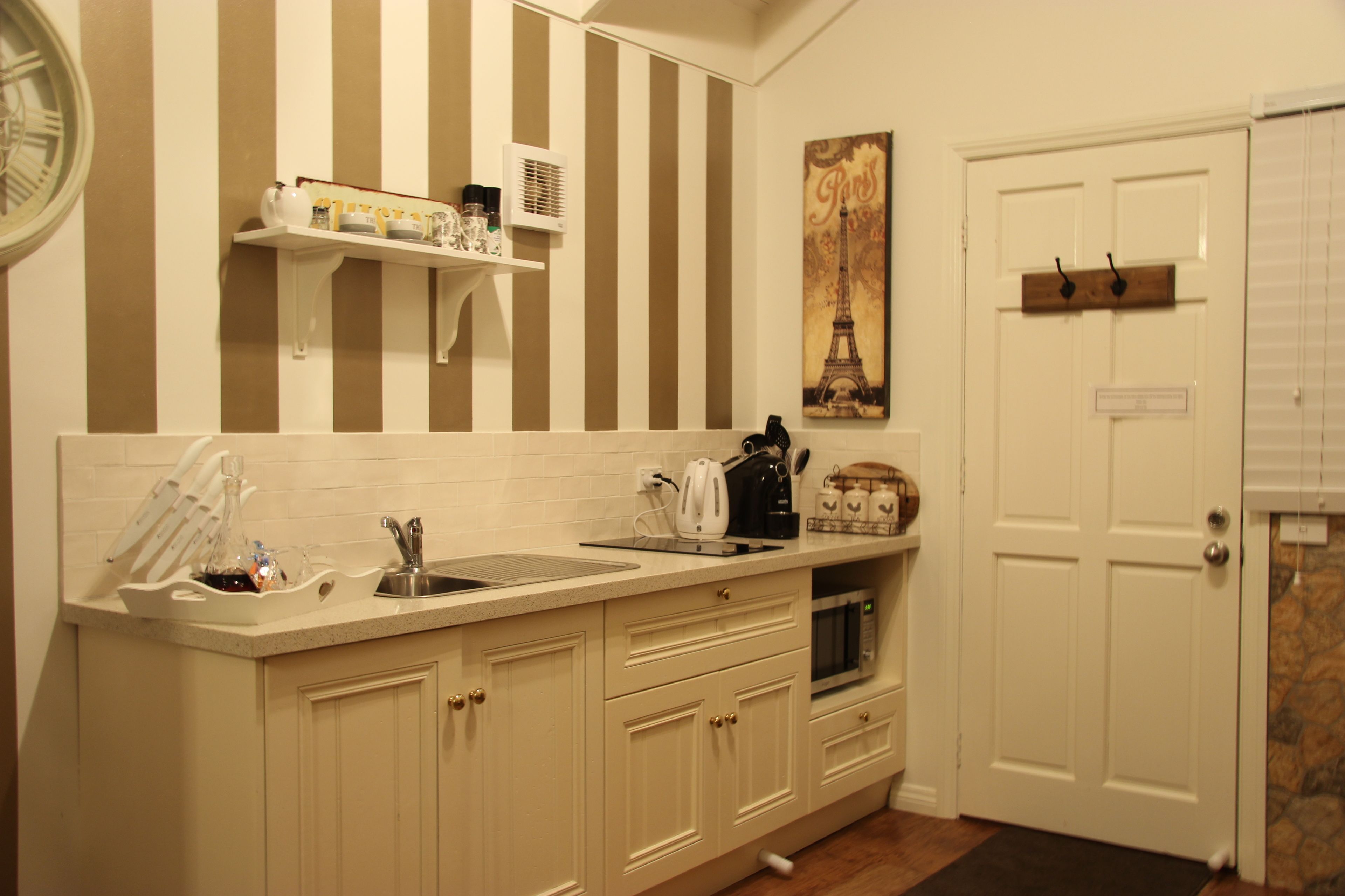 A kitchen with a striped wall, a white door, and a painting of the Eiffel Tower.