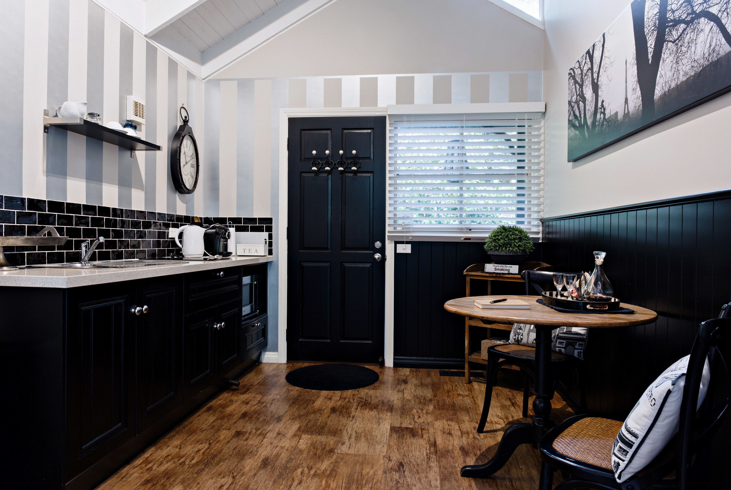 A kitchen with black cabinets, a wooden countertop, a black door, and a dining area with a round table and chairs.