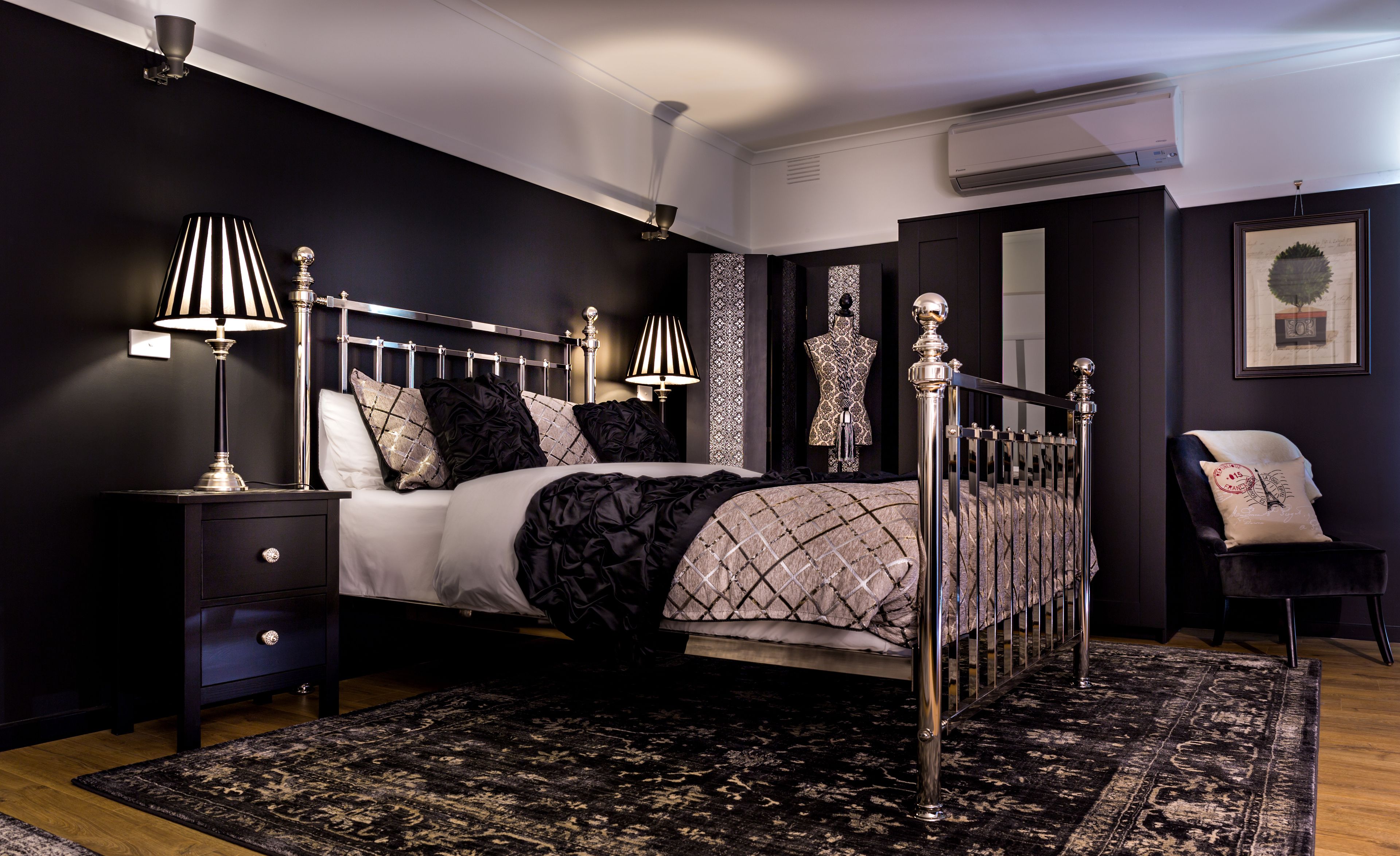 Een moderne slaapkamer met een groot bed, donkere muren en een kamerkleed met een patroon.