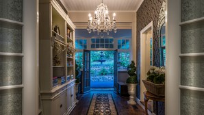 A hallway with a chandelier, open doors leading to a garden, and shelves with decorative items. - Belle Le Vie (Sassafras)