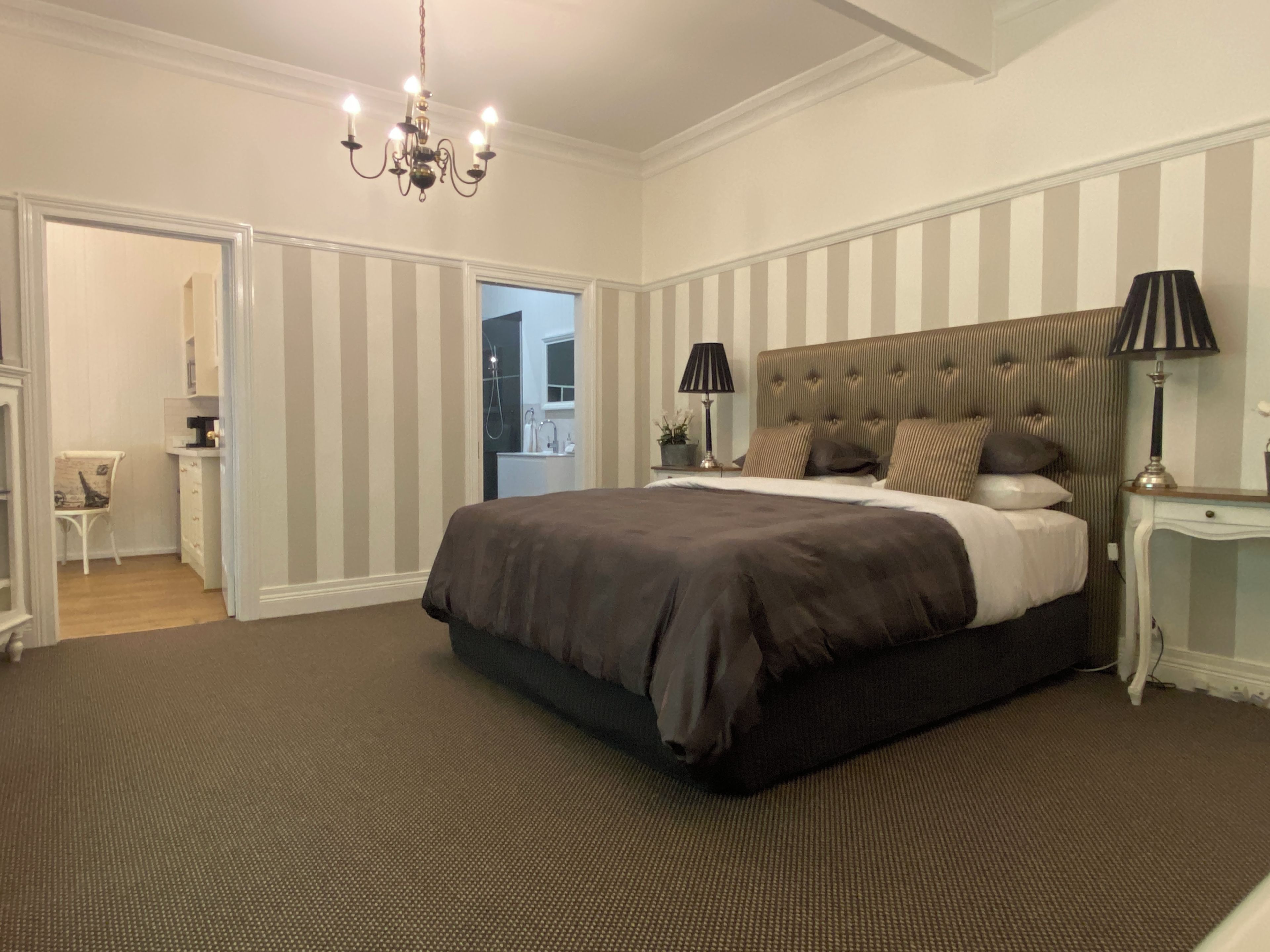 A bedroom with a large bed, two bedside tables with lamps, a chandelier, and a striped wall.