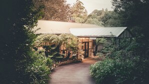 A pathway leading to a building with a stone facade and a metal roof, surrounded by lush greenery. - Belle Le Vie (Sassafras)