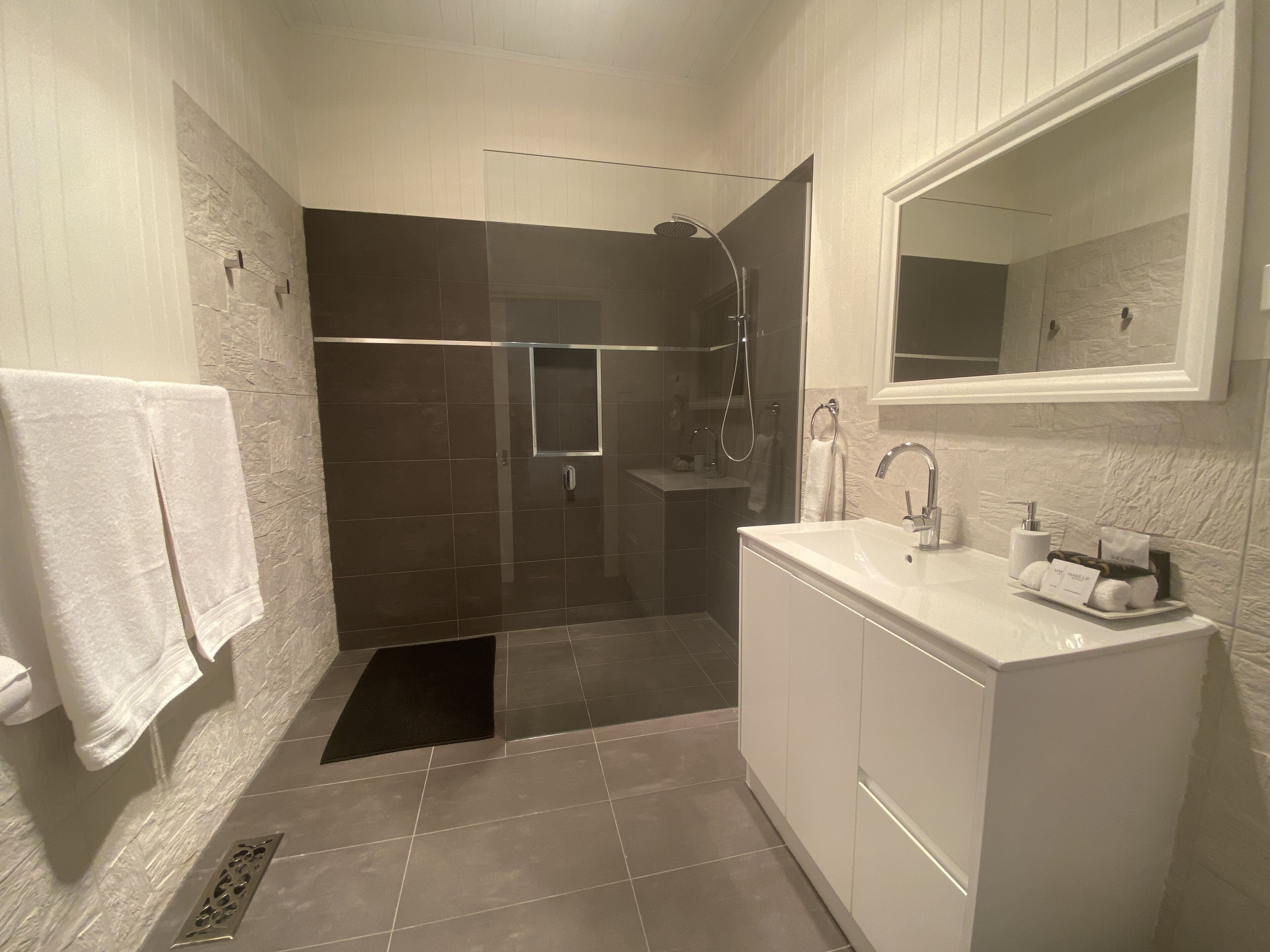 Een moderne badkamer met een douche in een glazen cabine, een wit wastafelmeubel met een spiegel en een handdoekhouder.