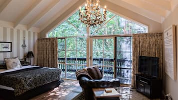 A bedroom with a large bed, a leather sofa, a TV, and a chandelier.