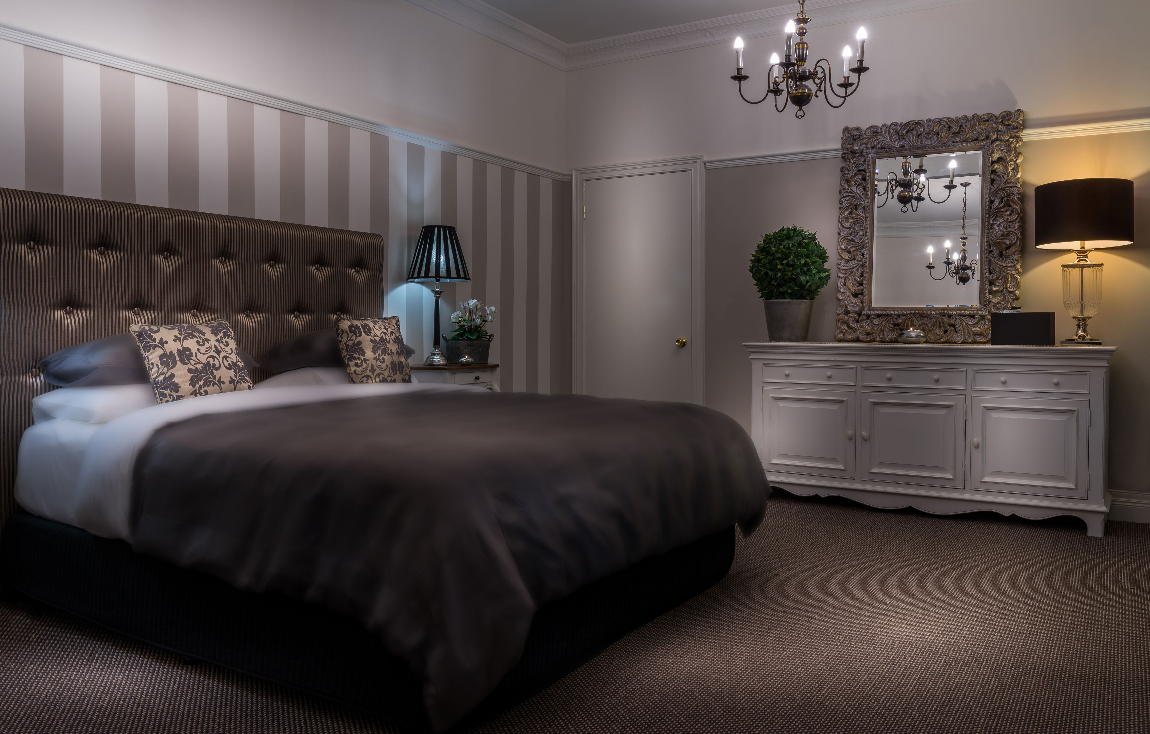 A bedroom with a large bed, a dresser, a mirror, and a chandelier.