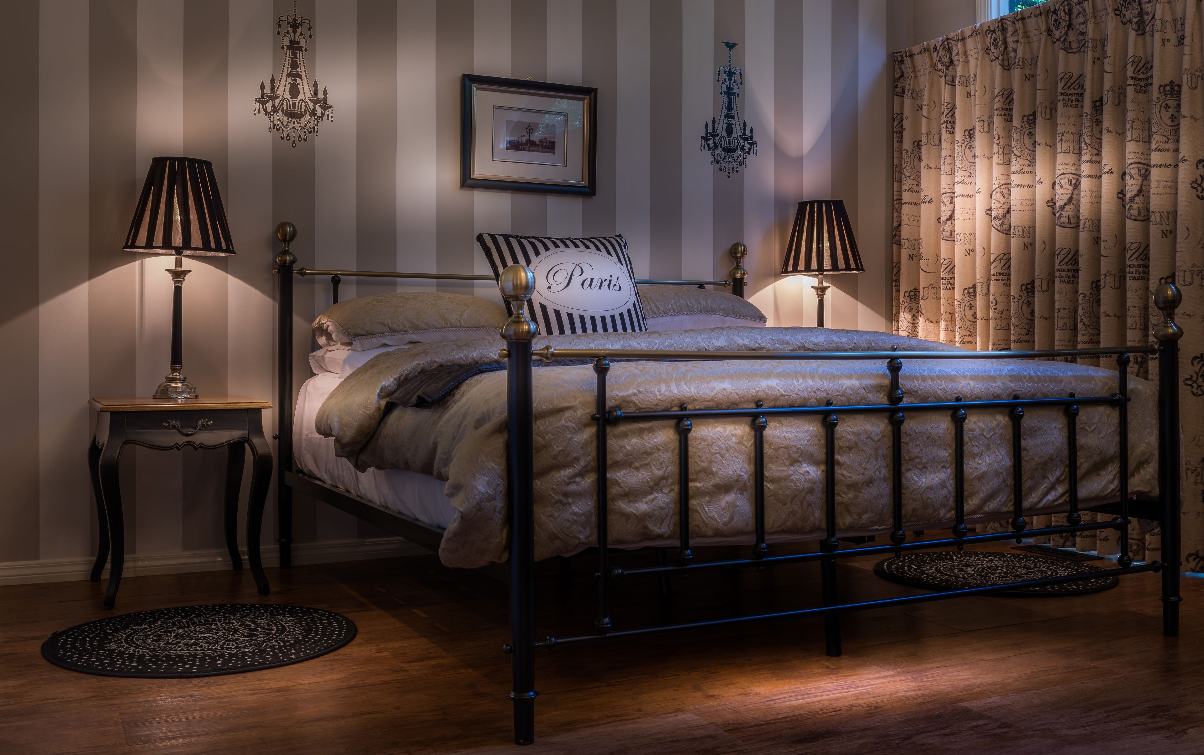 A neatly arranged bedroom with a metal bed frame, striped wallpaper, and a chandelier.