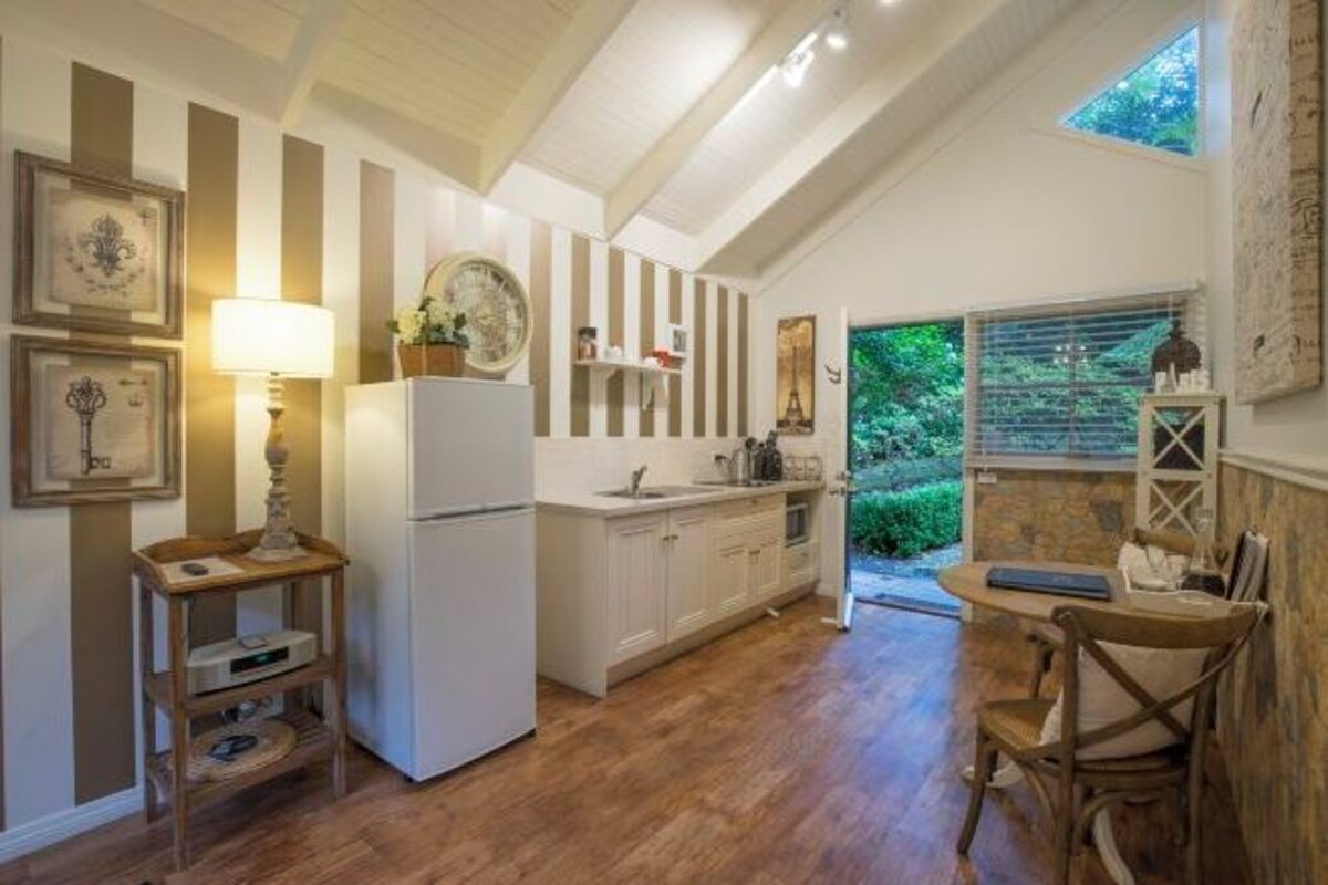 A kitchen with white cabinets, a refrigerator, a wooden table with chairs, and a window overlooking greenery.