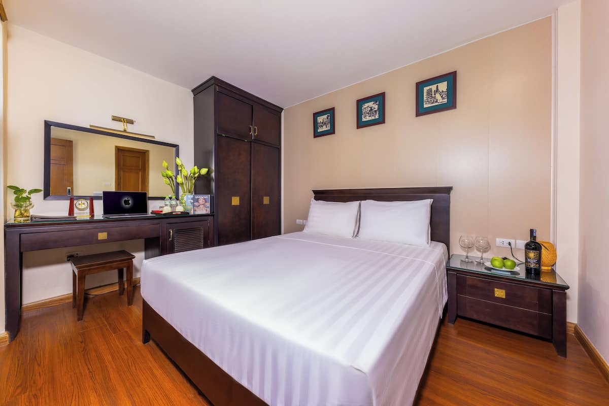 A neatly arranged hotel room with a large bed, a wooden desk with a computer, a mirror, and a wardrobe.