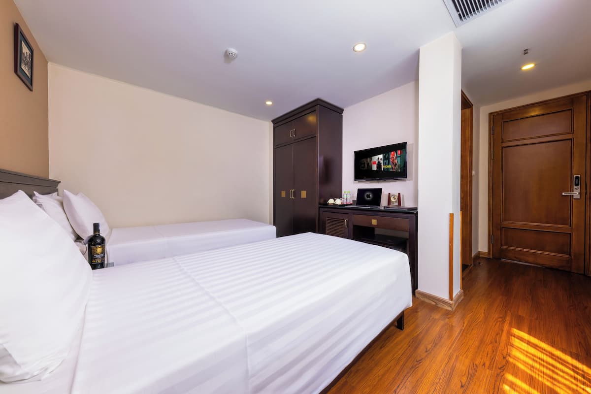 A hotel room with two beds, a desk with a computer, a television, and a wardrobe.