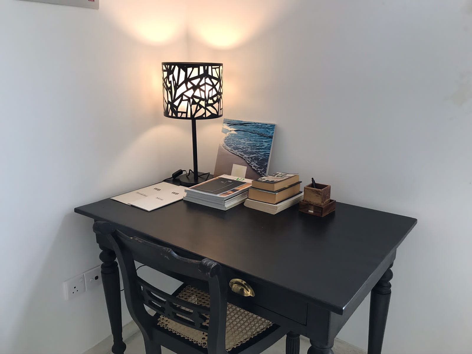 Un bureau en bois foncé, sur lequel se trouvent une lampe, des livres et un tableau encadré.