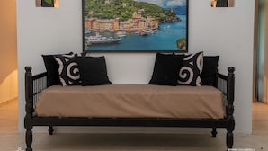 A bed with a beige cover, black frame, and two black pillows with white swirls. A framed painting of a coastal town is above the bed. - WB Villa (Unawatuna)