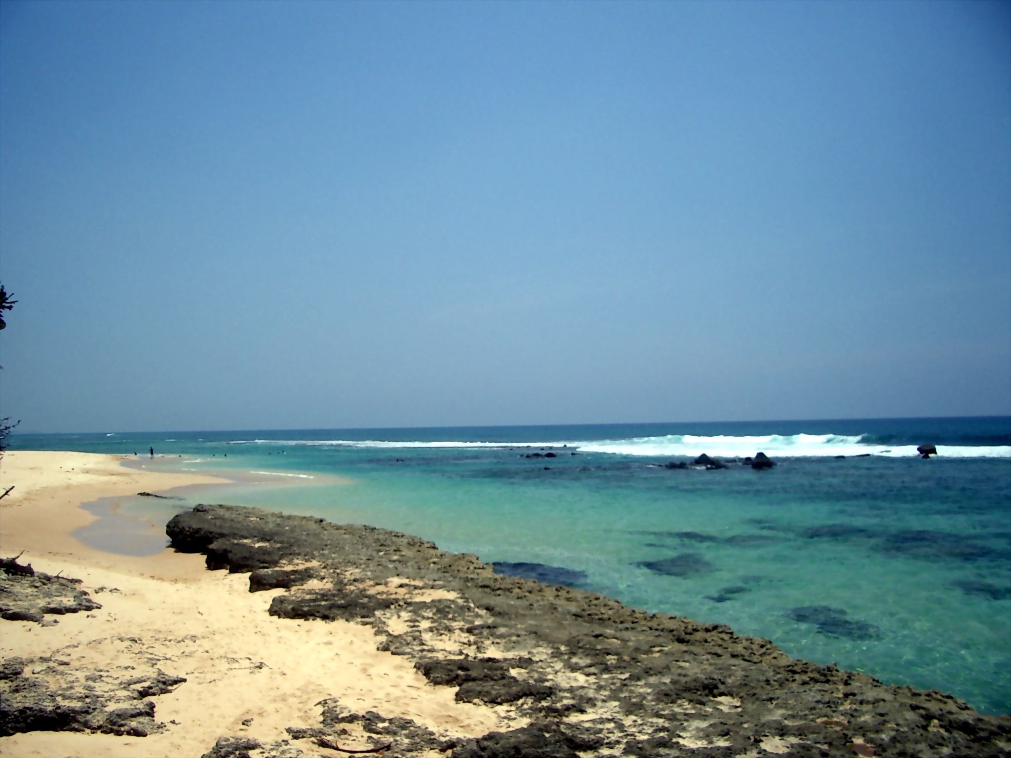 A beach with clear turquoise water, a sandy shore, and rocky outcrops.