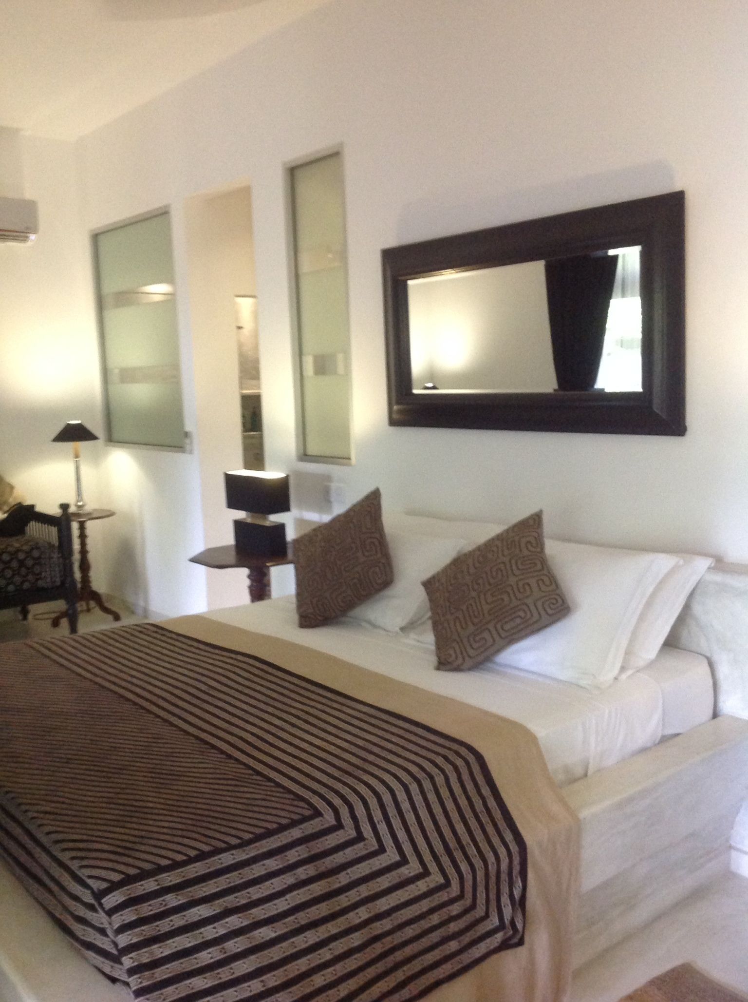 A hotel room with a bed, a large mirror, and a small table with a lamp.