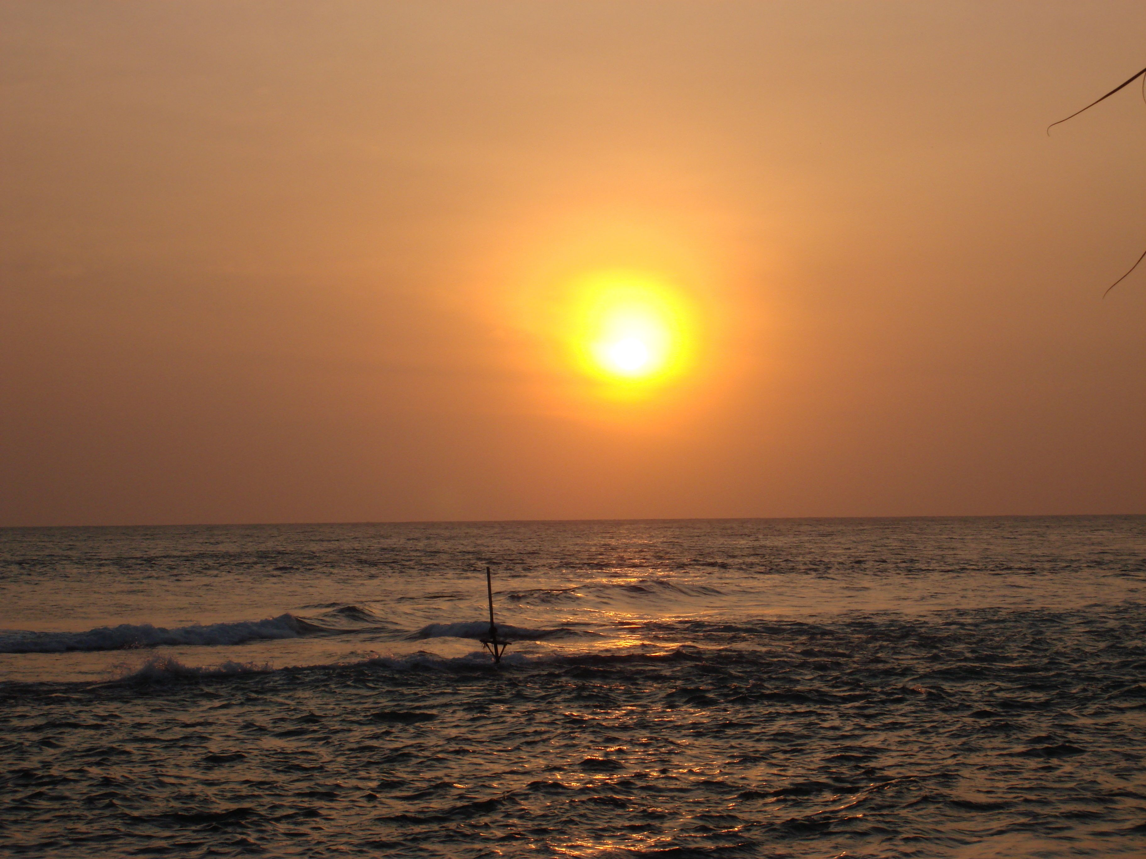 Un atardecer sobre el océano con olas y un único poste en primer plano.