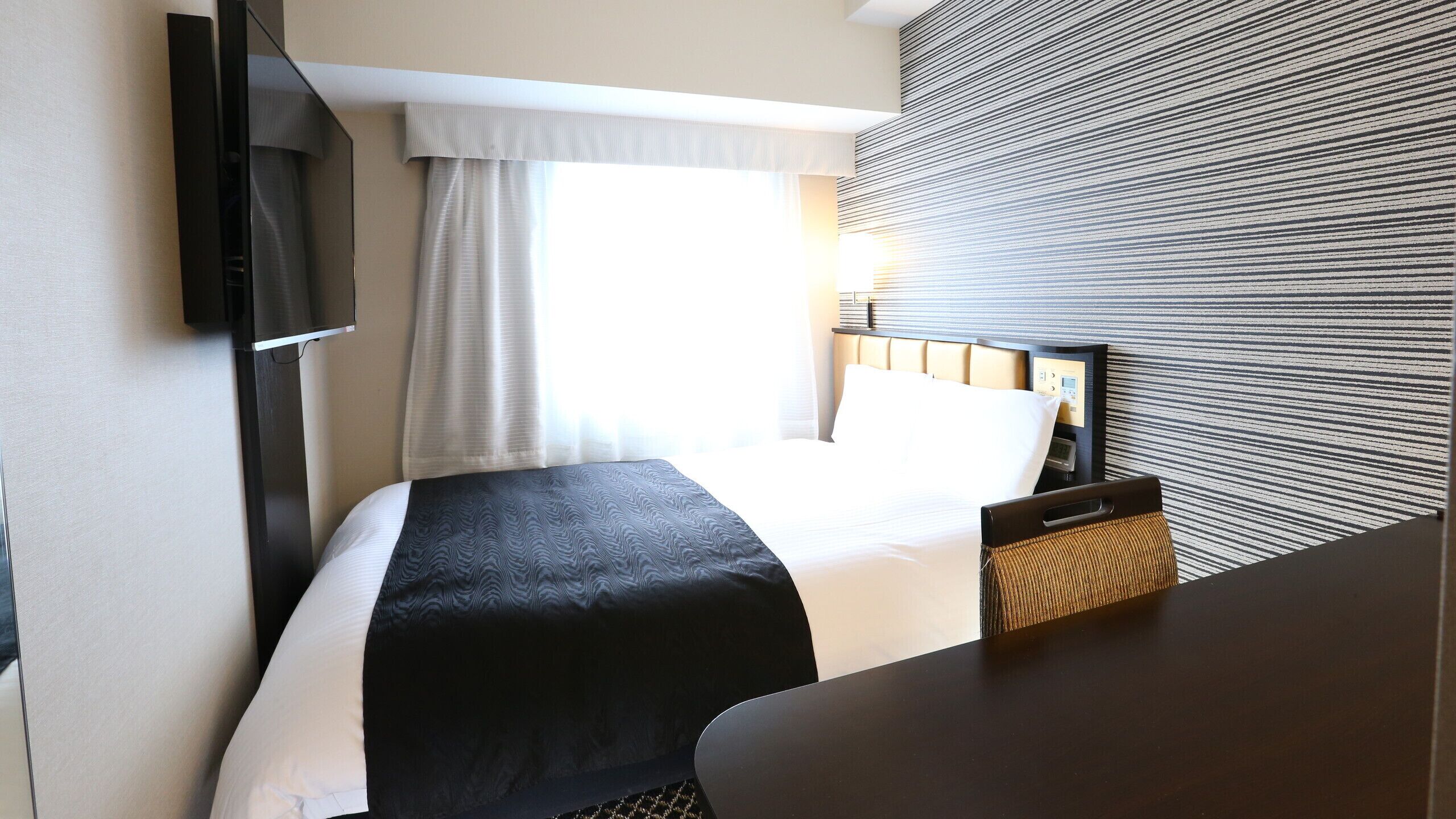Ein Hotelzimmer mit Bett, Wandfernseher, Schreibtisch und einem Vorhangfenster.