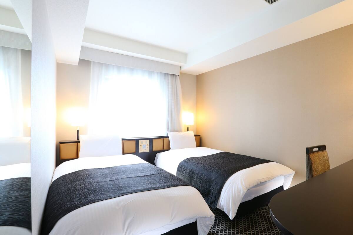 Une chambre d’hôtel avec deux lits, un bureau et une chaise.