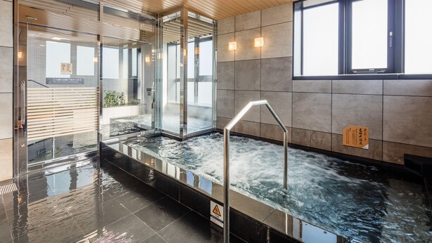 Un espace piscine intérieur moderne, doté de murs en verre, d’un plafond en bois et d’un sol carrelé.