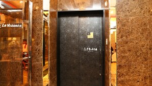 Un ascenseur avec un mur en marbre et une porte ornée de symboles d’accessibilité.