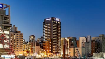 A high-rise building with "APA HOTEL" signage, surrounded by construction cranes and other buildings.